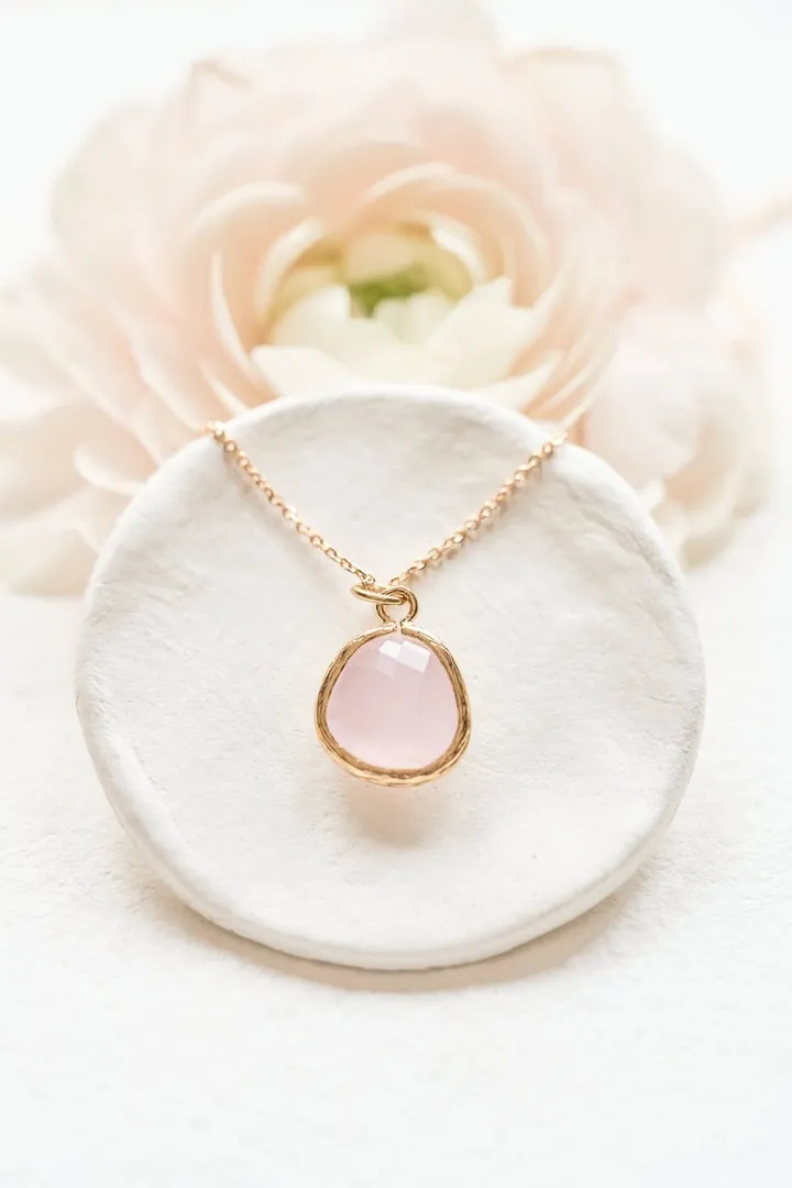 Collier à pendentif rose posé sur une coupelle blanche, fleur en arrière-plan