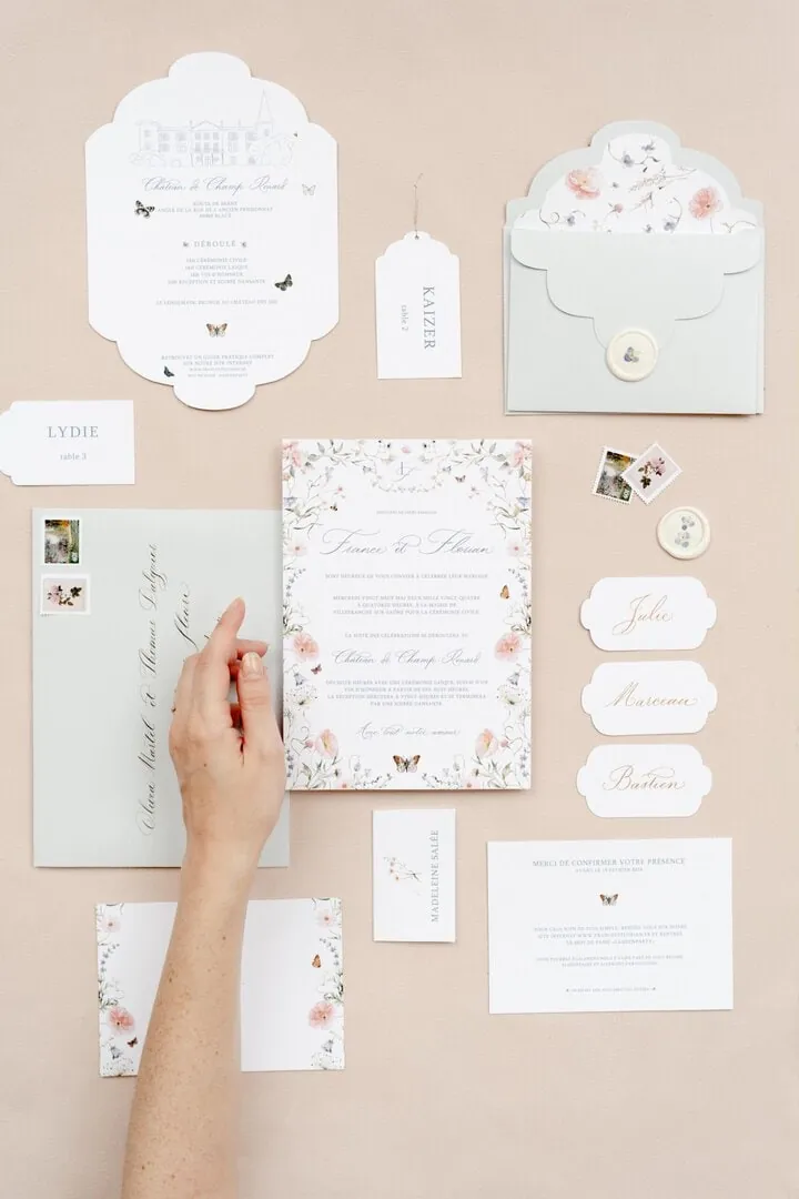 Papeterie de mariage disposée à plat, une main de graphiste ajustant un faire-part